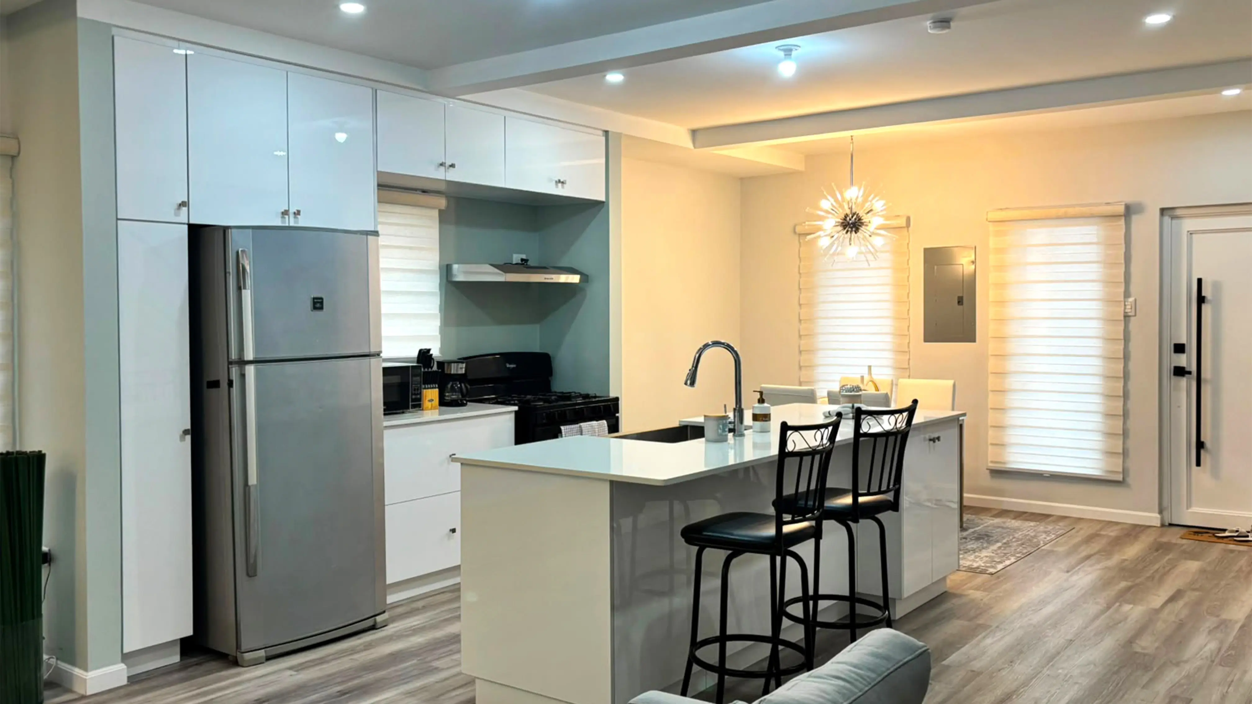 Kitchen with tall white cabinets, silver refrigerator and island breakfast bar, looking towards the dining area and front door.