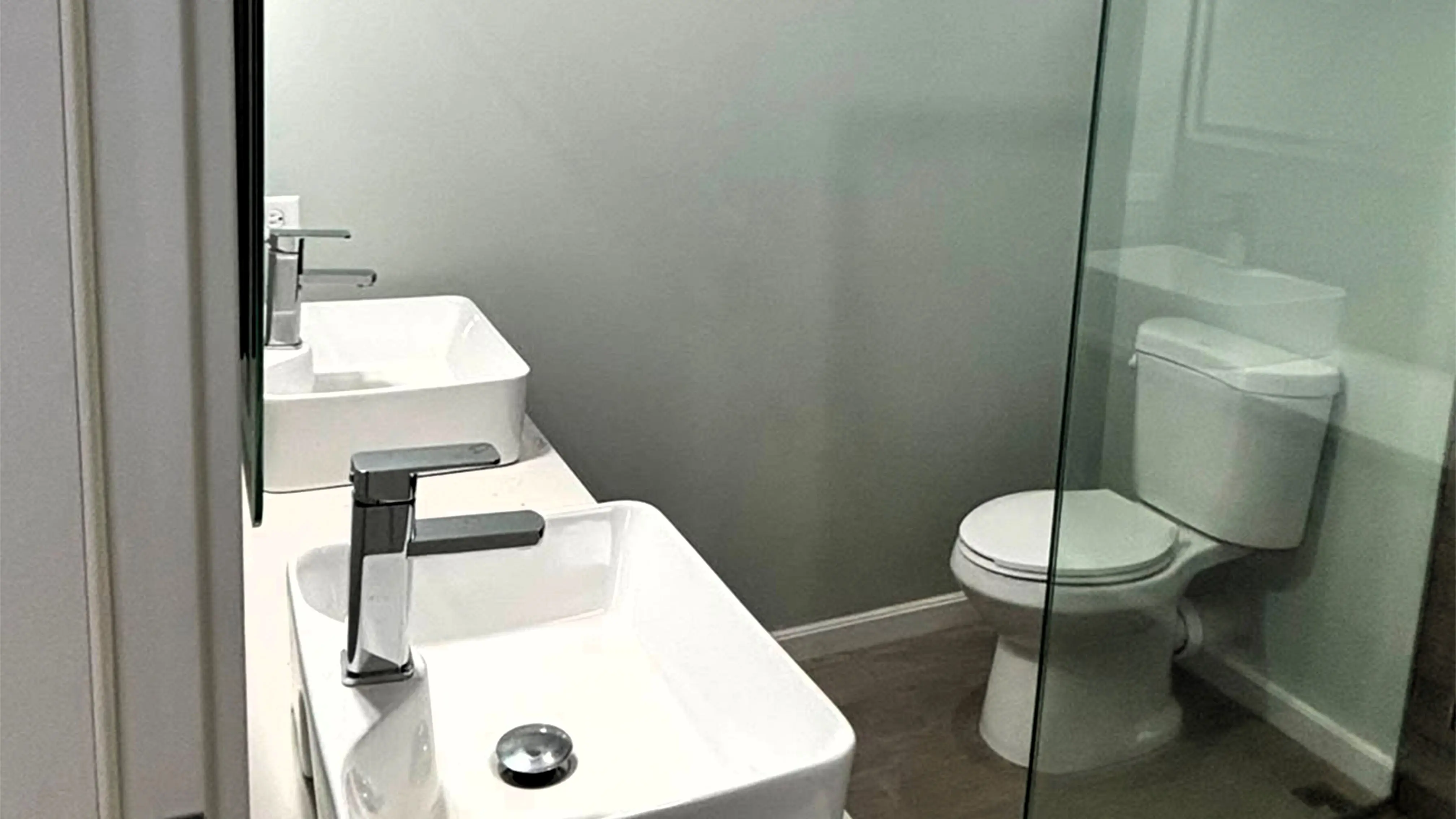 Bathroom with two white vessel sinks and chrome taps on a shared countertop, a toilet and a glass shower screen.