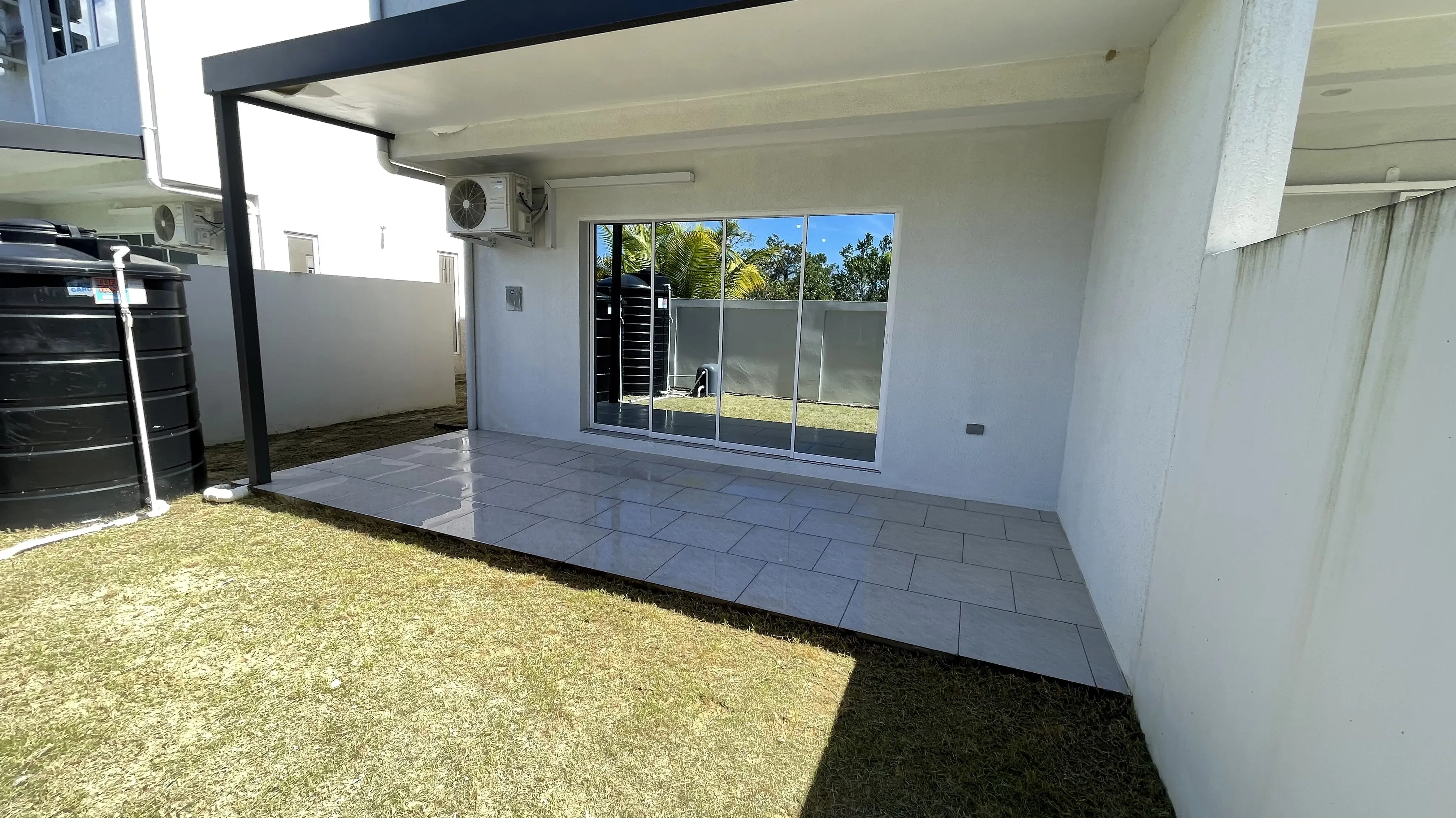 Covered tiled patio with wide sliding glass doors opening onto a lawn enclosed by boundary walls.