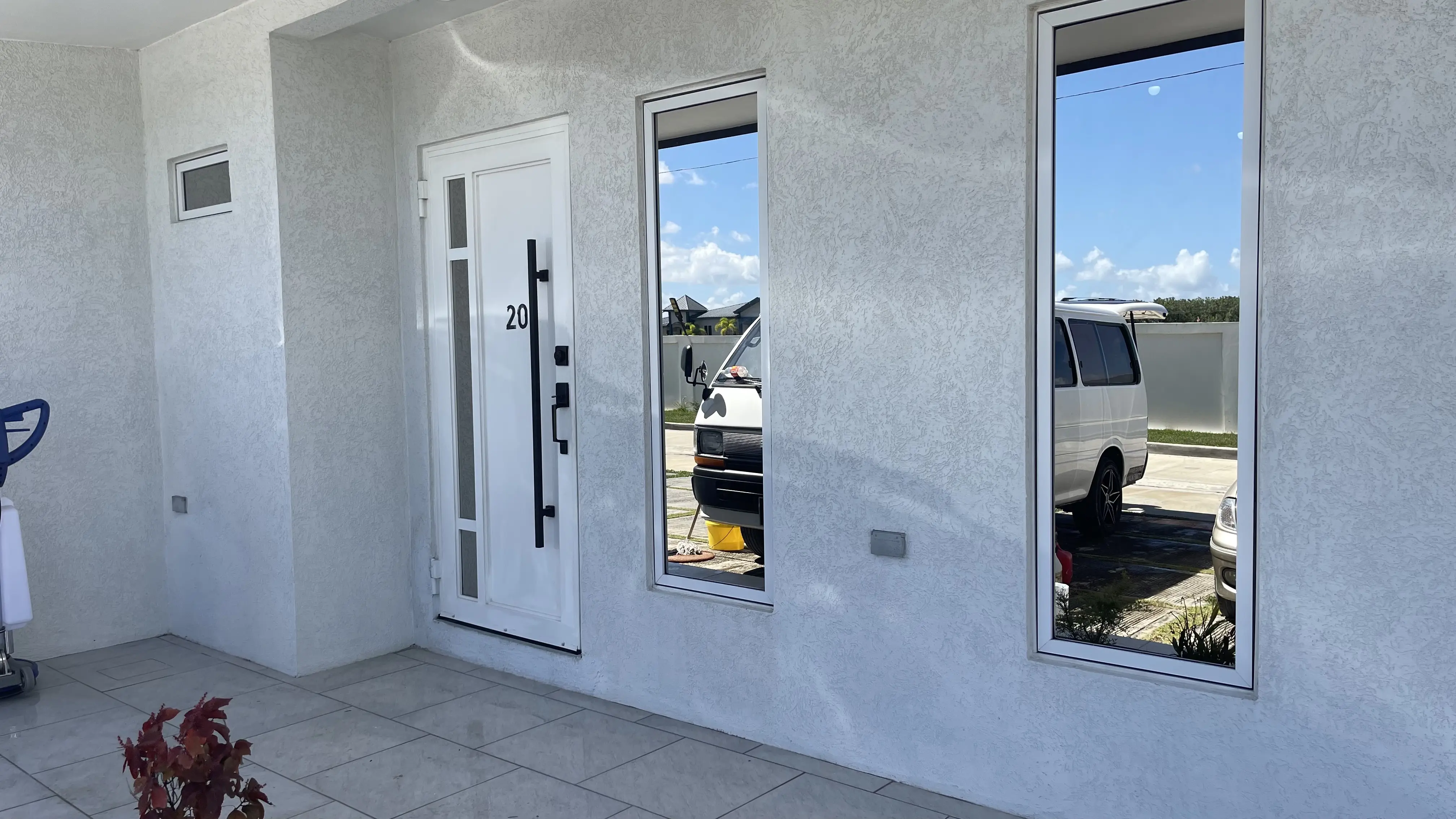 Covered entrance to the La Sierra townhouse with a white door marked 20, tall reflective windows and a tiled porch.